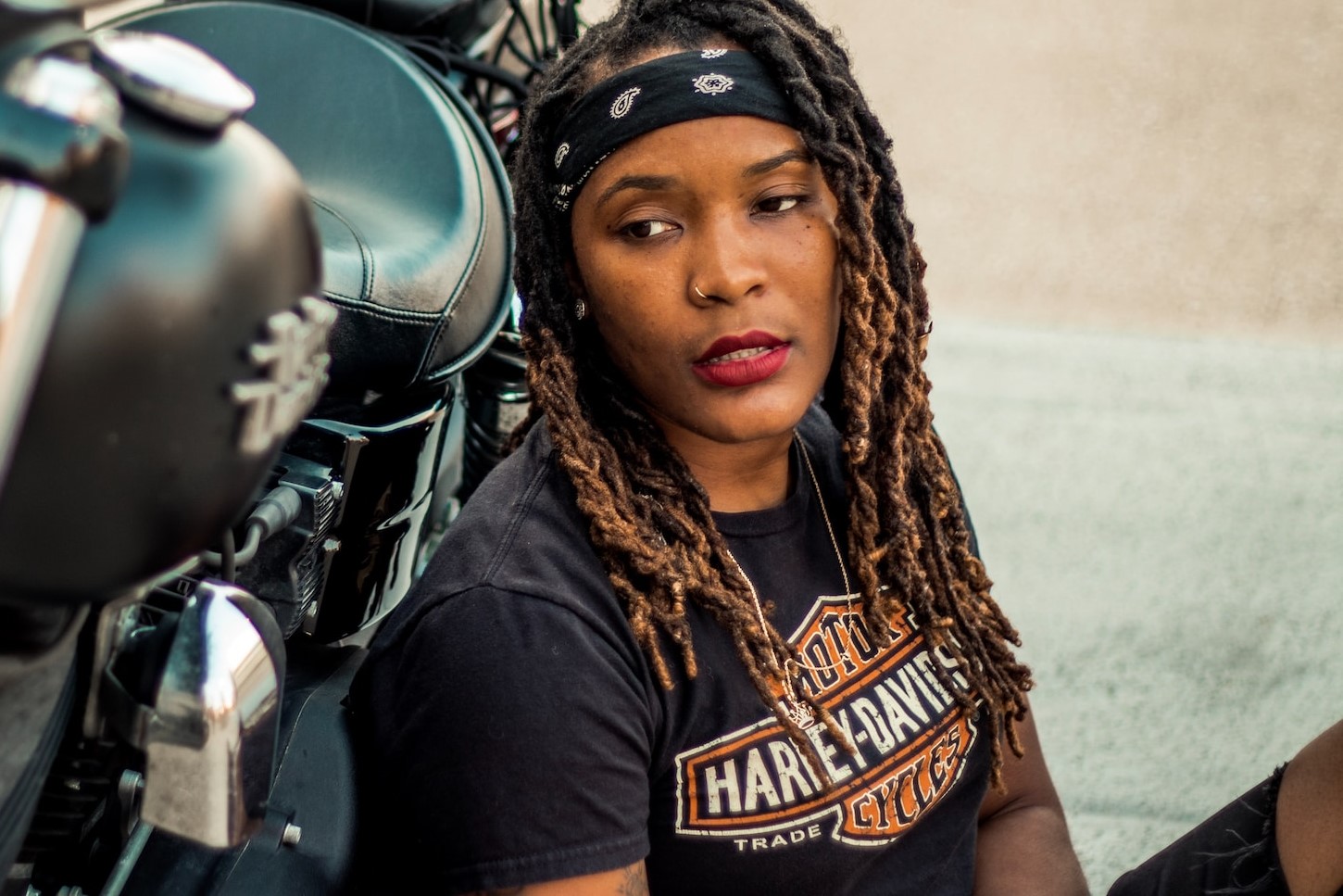 A woman wearing a Harley Davidson Clothes- a Harley Davidson T-shirt leaning up on a Harley Davidson bike