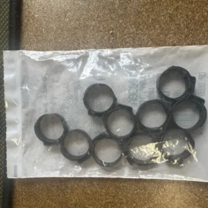 Clear plastic bag containing multiple small black rubber O-rings or seals laid out on a brown textured surface.