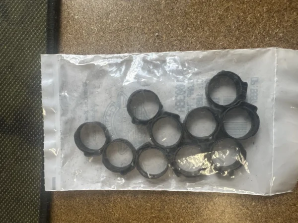 Clear plastic bag containing multiple small black rubber O-rings or seals laid out on a brown textured surface.