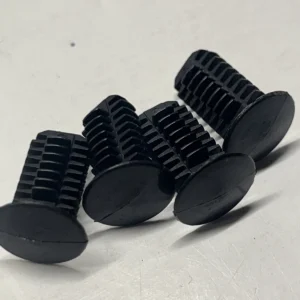 Close-up of several small black plastic gears with external teeth and flat circular bases resting on a light surface, arranged in a row.