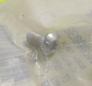 Metal bolt inside a clear plastic bag with a barcode visible in the background.