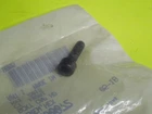 Small black screw placed on a clear plastic bag lying on a bright lime-green surface.