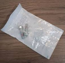Clear plastic bag containing a few metal screws on a wooden surface.