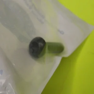 Green capsule partially inside white packaging on a bright yellow surface, close-up view.
