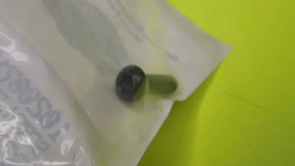 Green capsule partially inside white packaging on a bright yellow surface, close-up view.