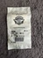 Small grayscale ticket or receipt showing a circular logo at the top, a few text lines, and a barcode at the bottom.