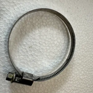 Circular metal hose clamp with a tightening screw on a textured white surface.