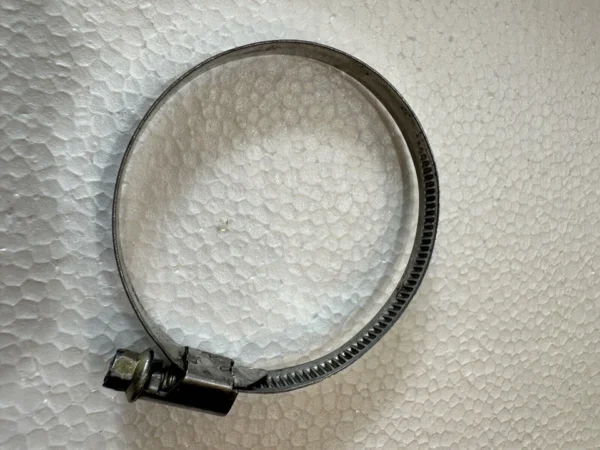 Circular metal hose clamp with a tightening screw on a textured white surface.