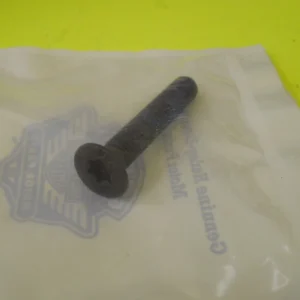 Close-up of a dark metal bolt lying on a translucent plastic bag on a bright yellow surface.