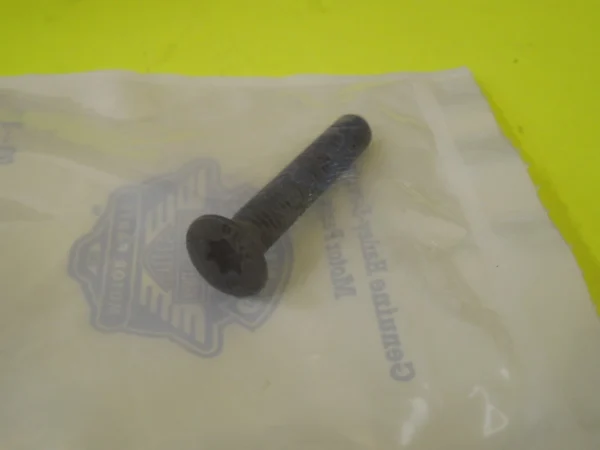 Close-up of a dark metal bolt lying on a translucent plastic bag on a bright yellow surface.