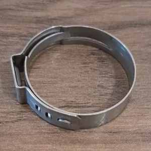 Circular metal hose clamp with a locking tab, laid on a wooden surface, showing adjustment holes.