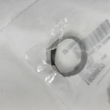 Close-up of a small circular ring inside a transparent plastic bag on a light surface, with the bag slightly crinkled around it.