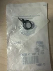 Small black plastic ring/clip sealed in a clear bag on a light wooden surface, item partly unfolded inside packaging.