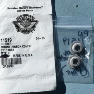 Harley-Davidson Genuine Motor Parts bag with part 11519 rubber mount airbox cover, next to a clear plastic bag containing two metal bushings on a blue surface.