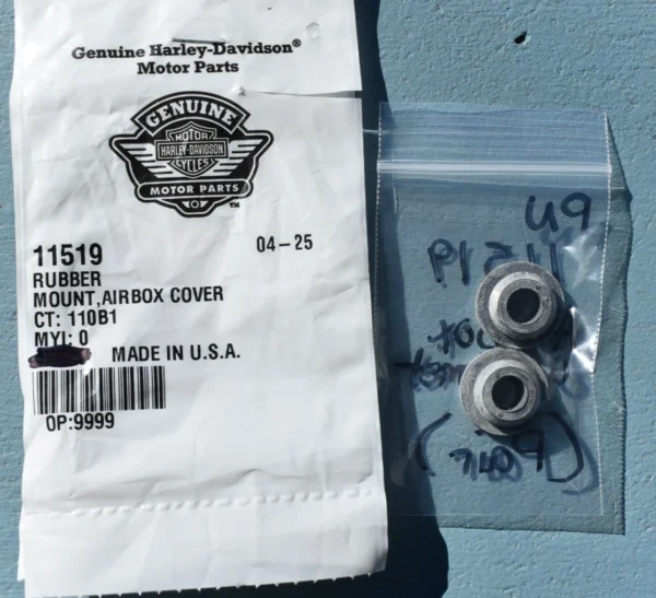11519 | Harley-davidson® Online Harley-Davidson Genuine Motor Parts bag with part 11519 rubber mount airbox cover, next to a clear plastic bag containing two metal bushings on a blue surface.