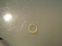 Gold ring with a small stone, placed on a scratched gray surface, photographed from above.