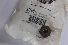 Small dark metal hex nut resting on a white plastic bag with a barcode and part number label.