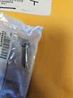 Small sealed plastic bag containing a metal hardware piece with a barcode label, placed on a yellow surface behind it.