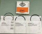 Three white paper tote bags with printed text hang by their handles on a green wall, with an orange sign bearing a logo above them.