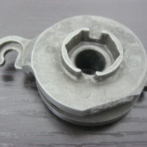 Gray plastic circular pulley-like part with a central opening and a small hooked tab on the side, on a dark wood surface.