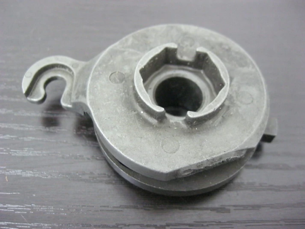 Gray plastic circular pulley-like part with a central opening and a small hooked tab on the side, on a dark wood surface.