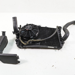 Automotive radiator with cooling fan and attached hoses on a white surface.