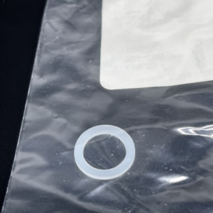 Small translucent circular washer on a crinkled black plastic bag near a white label.