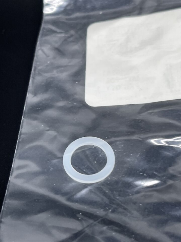Small translucent circular washer on a crinkled black plastic bag near a white label.