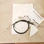 Black circular bracelet with a thin cord on a light beige surface, tag attached for product listing