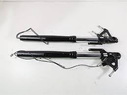 Two black gas springs with mounting brackets on a white surface, used to assist opening and hold a hatch or cabinet door.