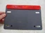 Small gray handheld device with a red top edge resting on a dark surface. It has four circular buttons along the lower side.