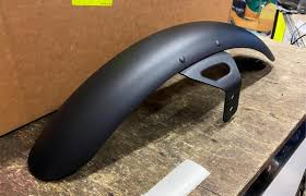 Black plastic fender with a mounting bracket on a wooden workbench in a workshop setting.