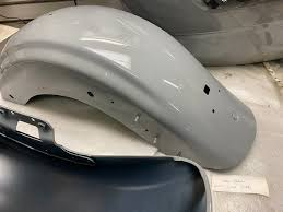 Gray car fenders placed on a workshop surface, with a dark blue bumper nearby.
