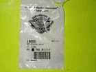 Clear plastic bag containing a small metal component with a barcode label, placed on a bright green surface (likely a spare part). Use for identifying a packaged hardware part.