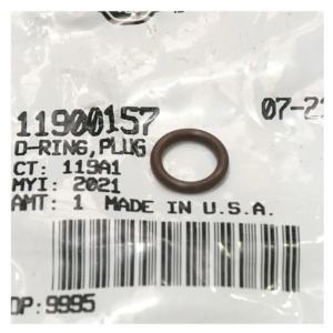 Close-up of a small brown O-ring resting on a plastic bag labeled 'O-RING, PLUG' with a barcode and part numbers visible.