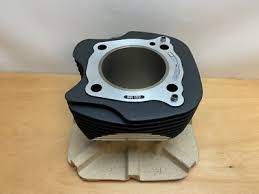 Aluminum engine cylinder block with cooling fins resting on a beige stand on a wooden table, showing the bore opening and bolt holes around the head gasket surface.