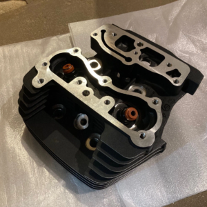 Motorcycle or small engine cylinder head with aluminum gasket, cooling fins, and orange valve seals placed on a protective sheet.