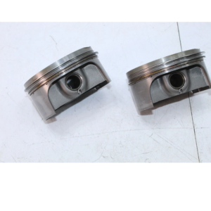 Two silver engine pistons lying side by side on a light surface, showing piston rings and pin holes.
