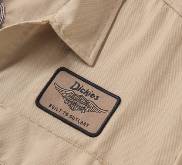 Close-up of a beige work shirt featuring a Dickies patch with wings and the words 'Built to Outlast' on tan fabric