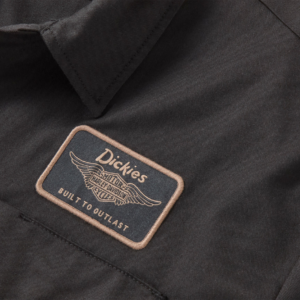 Close-up of a black work jacket with a beige-bordered Dickies patch reading 'Built to Outlast' and a winged logo.