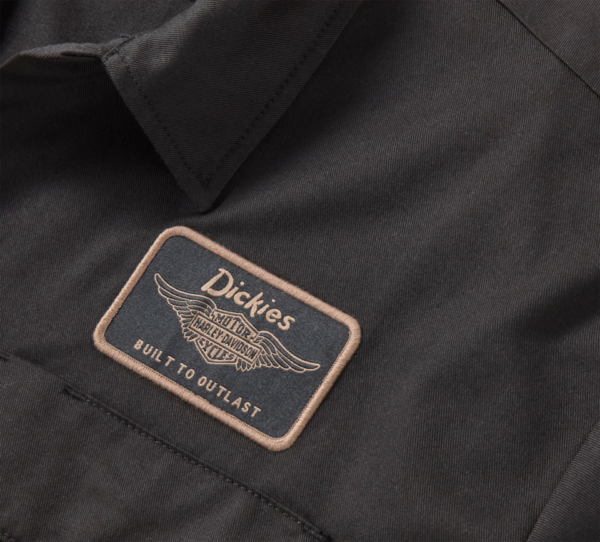 Close-up of a black work jacket with a beige-bordered Dickies patch reading 'Built to Outlast' and a winged logo.