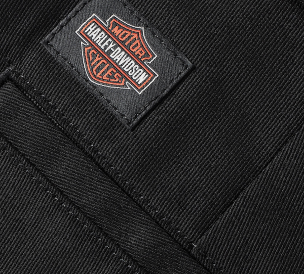 Close-up of black denim fabric with a Harley-Davidson patch sewn onto the pocket edge.