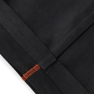 Close-up of black denim fabric with orange topstitching along a seam, highlighting reinforced stitching.