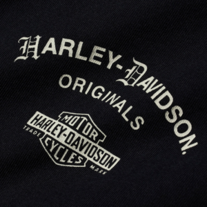 Close-up of black denim with white Harley-Davidson Originals logo and shield badge reading 'Motor Harley-Davidson Cycles'
