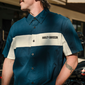 Man wearing a teal Harley-Davidson short-sleeve shirt with a white chest stripe and logo, outdoors.