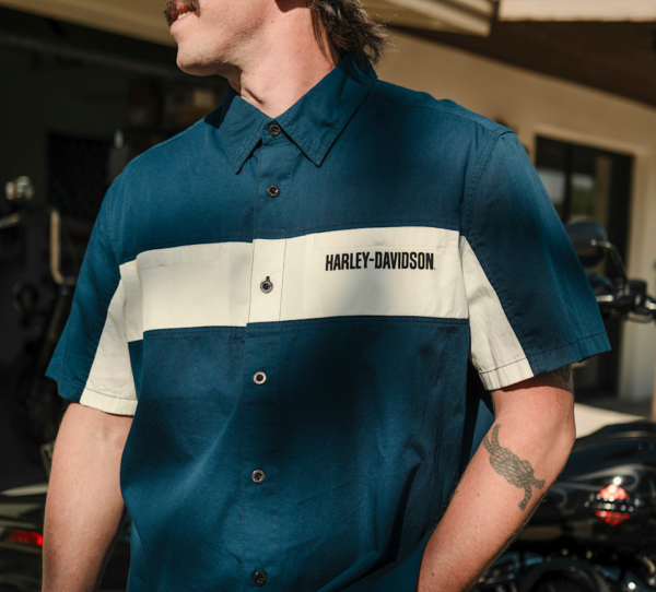 Man wearing a teal Harley-Davidson short-sleeve shirt with a white chest stripe and logo, outdoors.