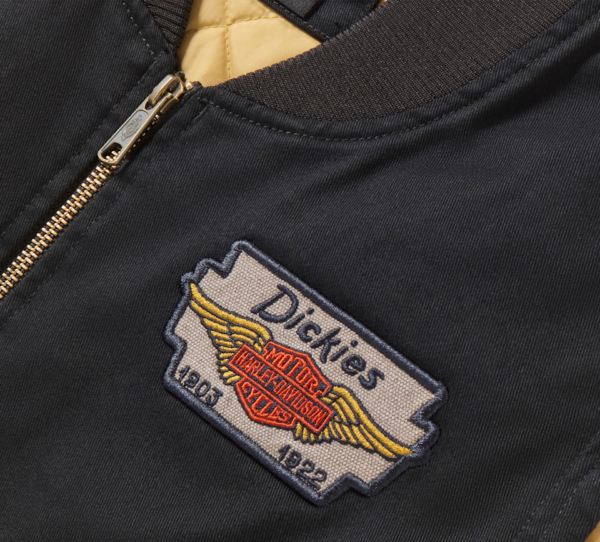 Close-up of a black jacket with a Dickies patch featuring wings and a Harley‑Davidson emblem.